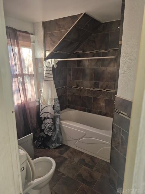 bathroom featuring tile walls, shower / bath combination with curtain, and toilet