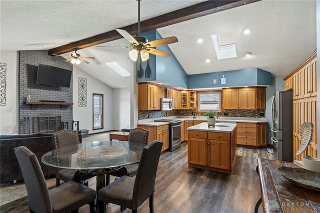 kitchen with a brick fireplace, dark hardwood / wood-style flooring, a kitchen island, stainless steel appliances, and vaulted ceiling with skylight