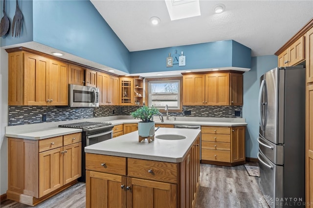 kitchen with light wood-type flooring, a kitchen island, lofted ceiling with skylight, and appliances with stainless steel finishes