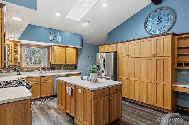 kitchen with lofted ceiling with skylight, sink, appliances with stainless steel finishes, dark hardwood / wood-style flooring, and a kitchen island with sink