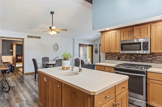 kitchen with sink, appliances with stainless steel finishes, a kitchen island with sink, backsplash, and vaulted ceiling