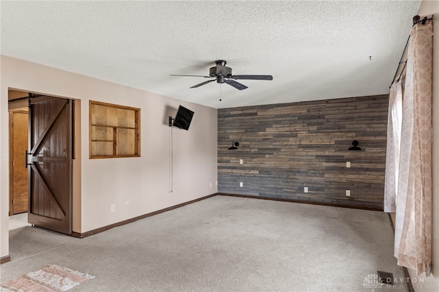 carpeted spare room featuring ceiling fan, a barn door, a textured ceiling, and wood walls