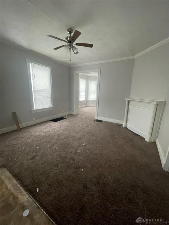 unfurnished living room featuring ceiling fan, ornamental molding, and dark carpet