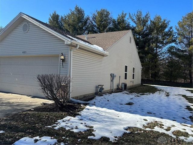 view of snowy exterior featuring a garage and central AC