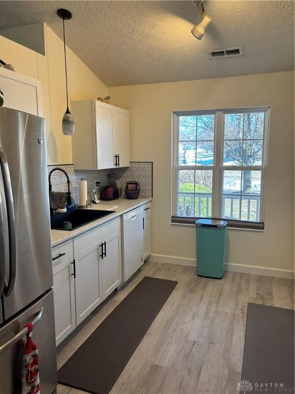 kitchen featuring white cabinetry, dishwasher, pendant lighting, and stainless steel refrigerator