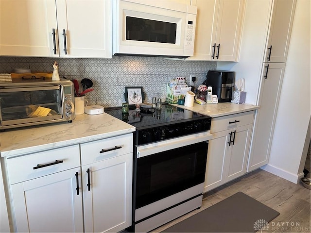 kitchen with white cabinetry, backsplash, light stone countertops, and electric range