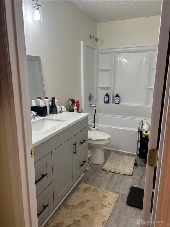 full bathroom featuring hardwood / wood-style flooring, bathing tub / shower combination, vanity, a textured ceiling, and toilet