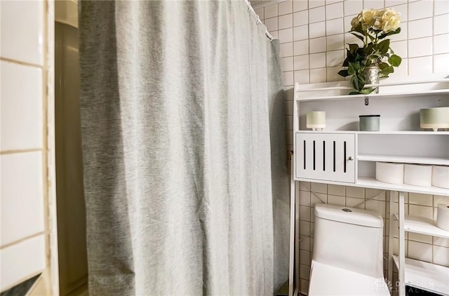 bathroom with tasteful backsplash, toilet, and tile walls