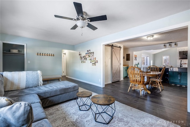 living area with a barn door, baseboards, dark wood finished floors, and a ceiling fan