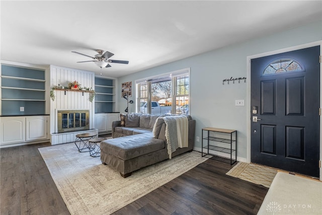 living room with dark hardwood / wood-style floors, a large fireplace, ceiling fan, and built in shelves