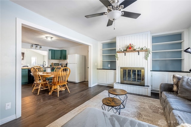 living area with built in features, a large fireplace, baseboards, and dark wood-type flooring