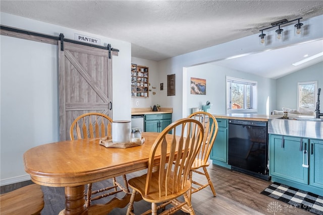 dining area featuring a barn door, vaulted ceiling, a textured ceiling, light wood-type flooring, and baseboards