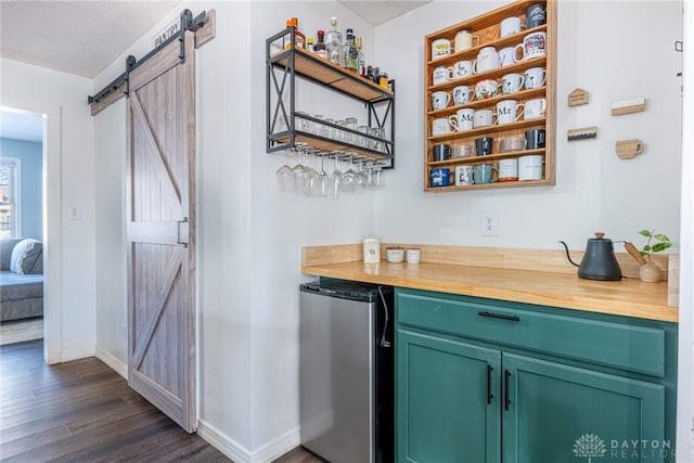 bar featuring a barn door, baseboards, dark wood finished floors, a bar, and fridge