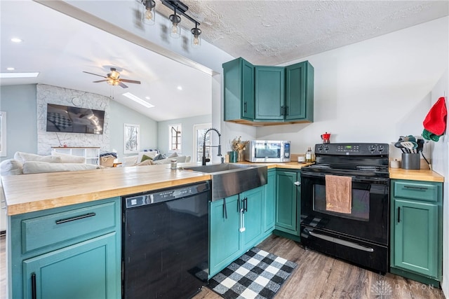 kitchen with open floor plan, a peninsula, vaulted ceiling, black appliances, and a sink