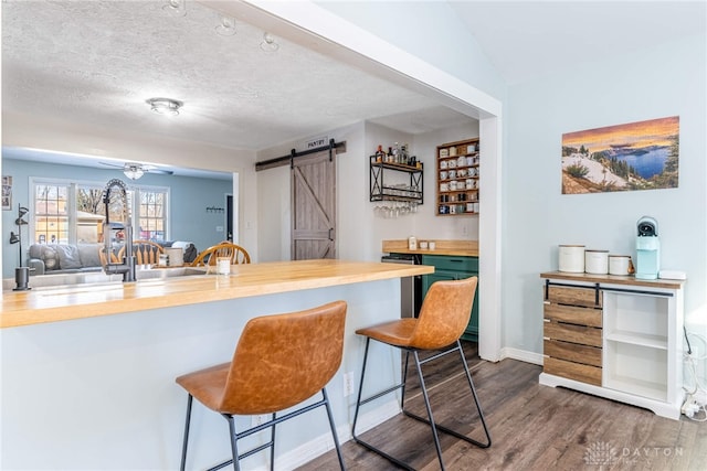 bar with a barn door, baseboards, dark wood finished floors, a ceiling fan, and a textured ceiling