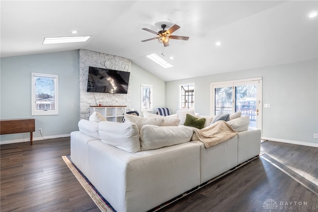 living room featuring vaulted ceiling with skylight, dark wood-style flooring, ceiling fan, and baseboards