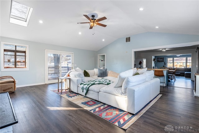 living area with dark wood-style floors, a wealth of natural light, lofted ceiling with skylight, and visible vents