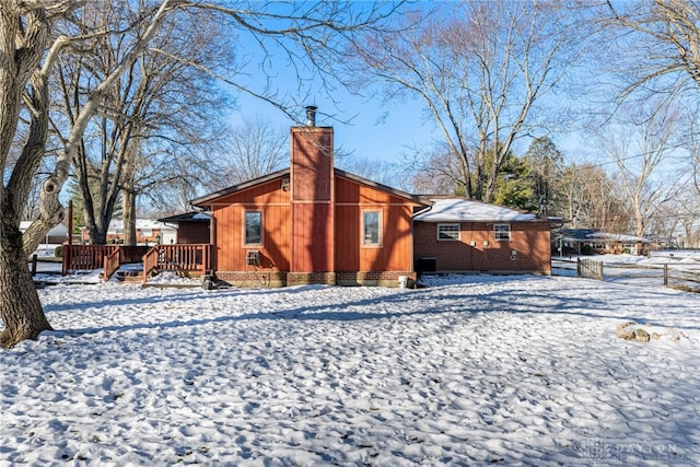 snow covered house featuring a chimney, a deck, and brick siding