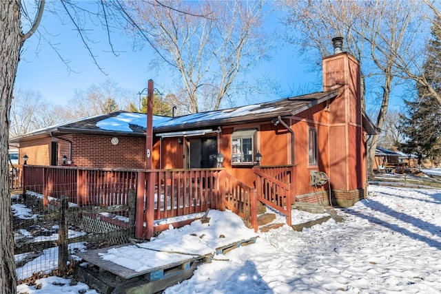 snow covered house featuring brick siding and a chimney