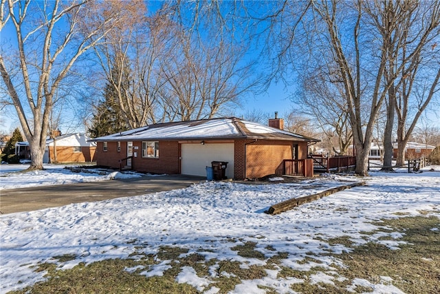 view of snow covered exterior featuring an attached garage, a wooden deck, a chimney, and brick siding