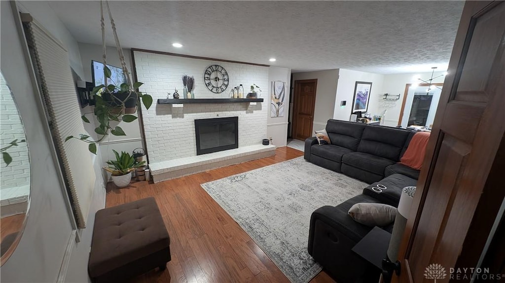 living room featuring a textured ceiling, a brick fireplace, and light wood-type flooring