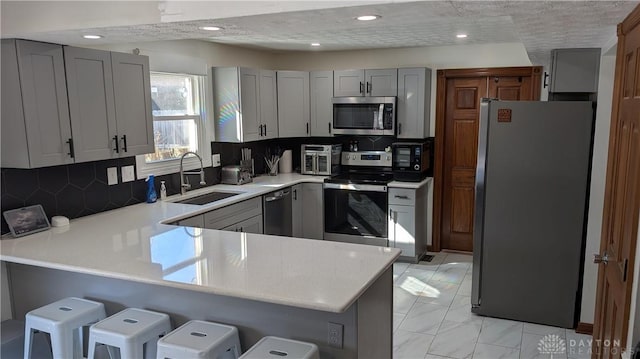 kitchen featuring sink, gray cabinetry, appliances with stainless steel finishes, a kitchen breakfast bar, and kitchen peninsula