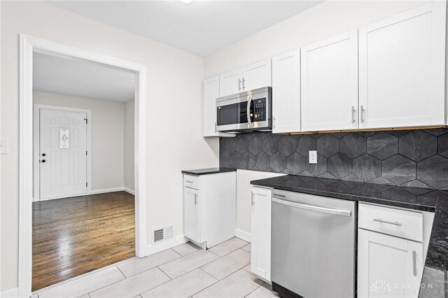 kitchen featuring light tile patterned flooring, tasteful backsplash, dark stone countertops, white cabinets, and stainless steel appliances