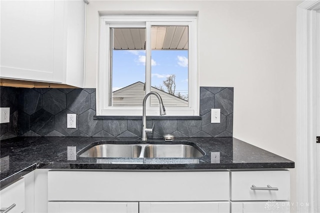 kitchen featuring white cabinetry, sink, decorative backsplash, and dark stone counters