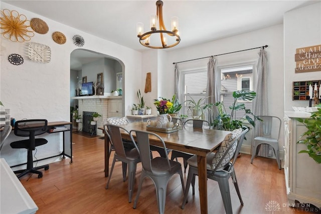 dining area with a brick fireplace, hardwood / wood-style flooring, and a notable chandelier