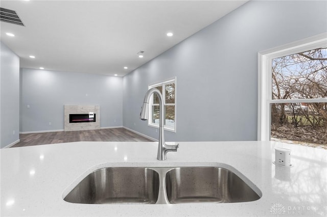 kitchen featuring plenty of natural light, light stone countertops, sink, and wood-type flooring