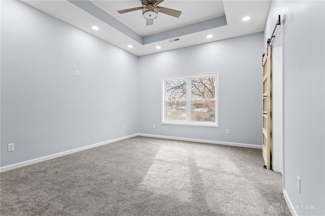 spare room with a raised ceiling, a barn door, ceiling fan, and carpet