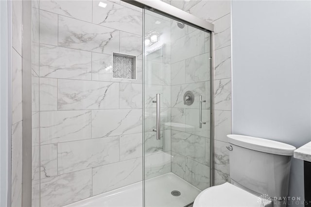 bathroom featuring a shower with door and toilet