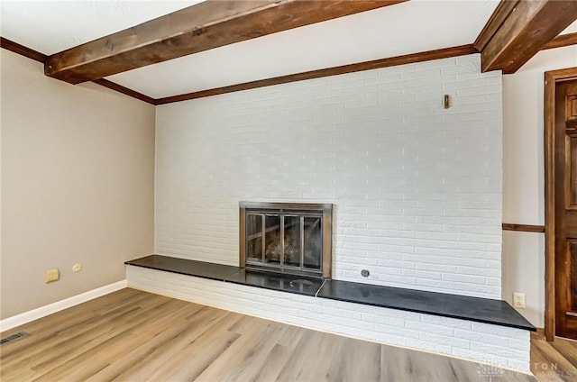 unfurnished living room featuring beamed ceiling, wood-type flooring, and a brick fireplace