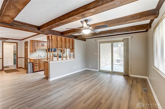 unfurnished living room featuring beamed ceiling, ceiling fan, sink, and light wood-type flooring