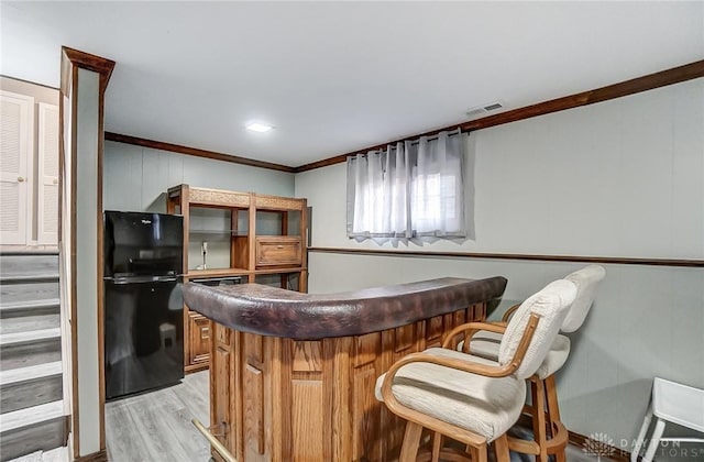 bar featuring crown molding, black refrigerator, and light wood-type flooring