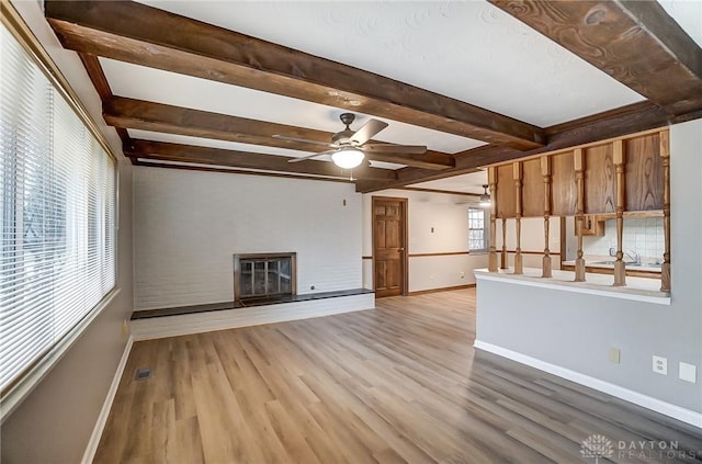 unfurnished living room featuring ceiling fan, beamed ceiling, and light wood-type flooring