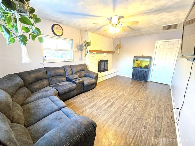 living room featuring hardwood / wood-style flooring, ceiling fan, and a brick fireplace