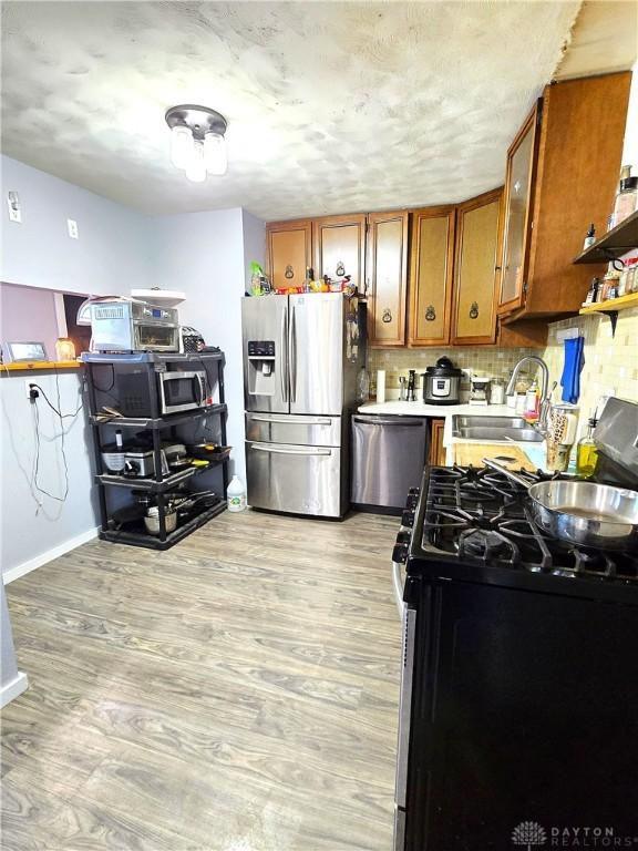 kitchen featuring decorative backsplash, stainless steel appliances, sink, and light hardwood / wood-style flooring