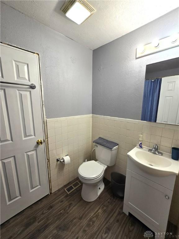 bathroom featuring toilet, wood-type flooring, a textured ceiling, tile walls, and vanity