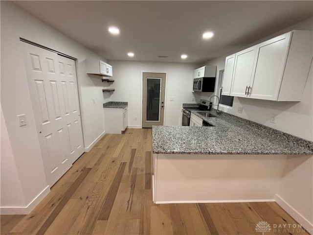 kitchen with stone counters, white cabinets, kitchen peninsula, stainless steel appliances, and light wood-type flooring