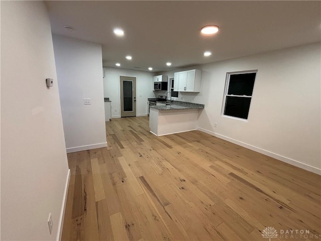 kitchen featuring appliances with stainless steel finishes, white cabinets, dark stone counters, light hardwood / wood-style floors, and kitchen peninsula