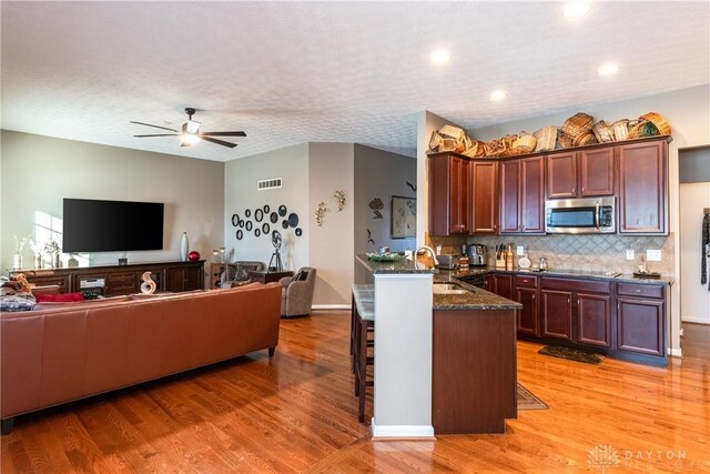 kitchen featuring sink, light hardwood / wood-style flooring, ceiling fan, dark stone counters, and backsplash