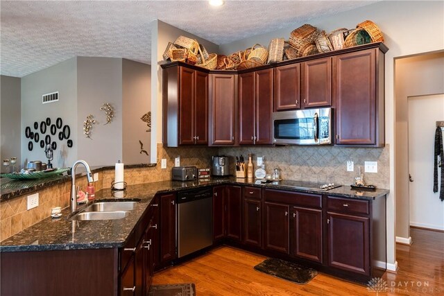 kitchen with sink, light hardwood / wood-style flooring, dark stone countertops, kitchen peninsula, and stainless steel appliances