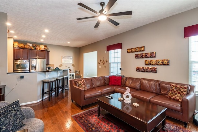 living room with dark wood-type flooring, ceiling fan, and a textured ceiling