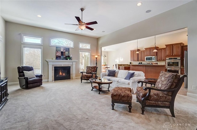 carpeted living room with ceiling fan, a tiled fireplace, and a high ceiling