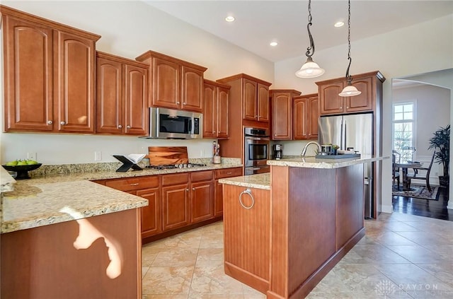 kitchen with decorative light fixtures, light stone countertops, an island with sink, and appliances with stainless steel finishes