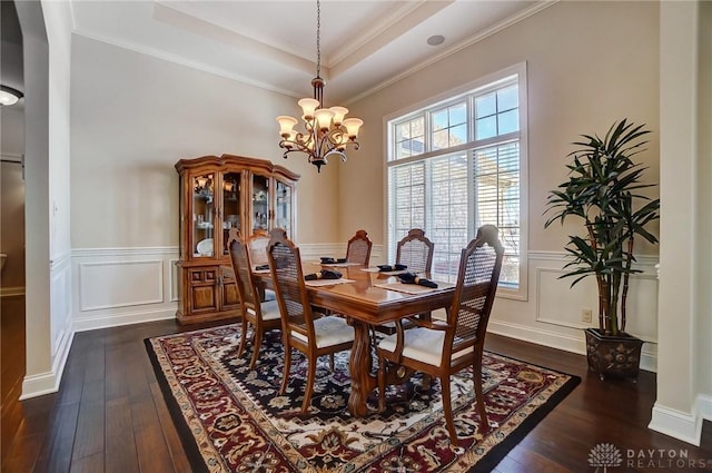 dining space featuring dark wood-type flooring, ornamental molding, a tray ceiling, and an inviting chandelier