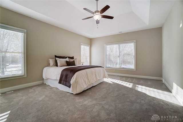 carpeted bedroom featuring multiple windows, a tray ceiling, and ceiling fan