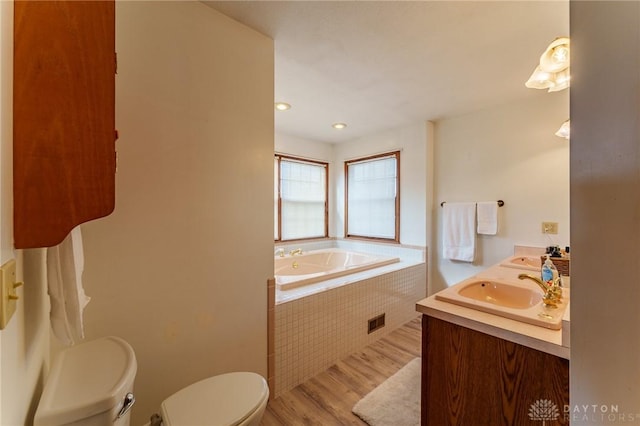 bathroom featuring hardwood / wood-style flooring, vanity, tiled bath, and toilet