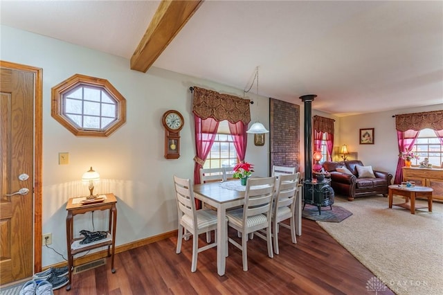 dining space featuring beamed ceiling, plenty of natural light, a wood stove, and dark wood-type flooring